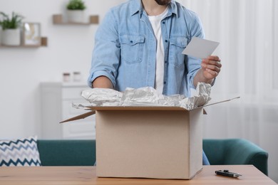 Man holding greeting card near parcel with Christmas gift, closeup