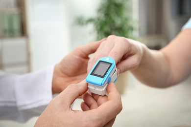 Photo of Doctor checking mature woman's pulse with medical device indoors, closeup