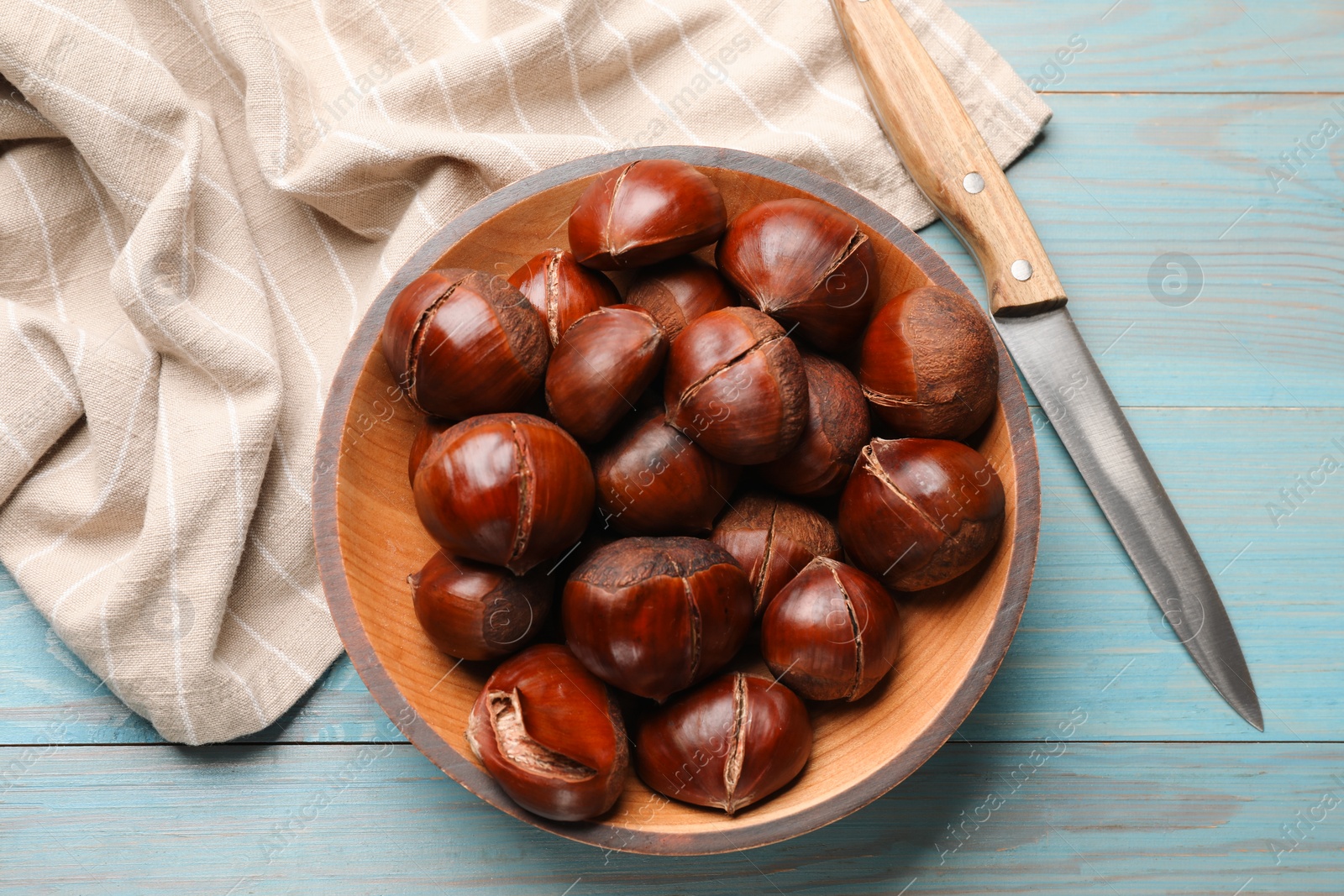 Photo of Fresh edible sweet chestnuts and knife on light blue wooden table, flat lay