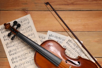 Violin, bow and music sheets on wooden table, top view