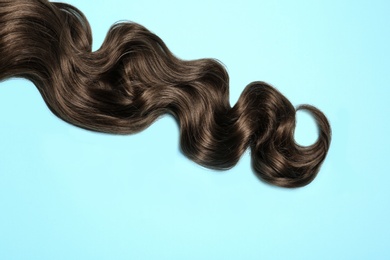 Lock of brown wavy hair on color background, top view