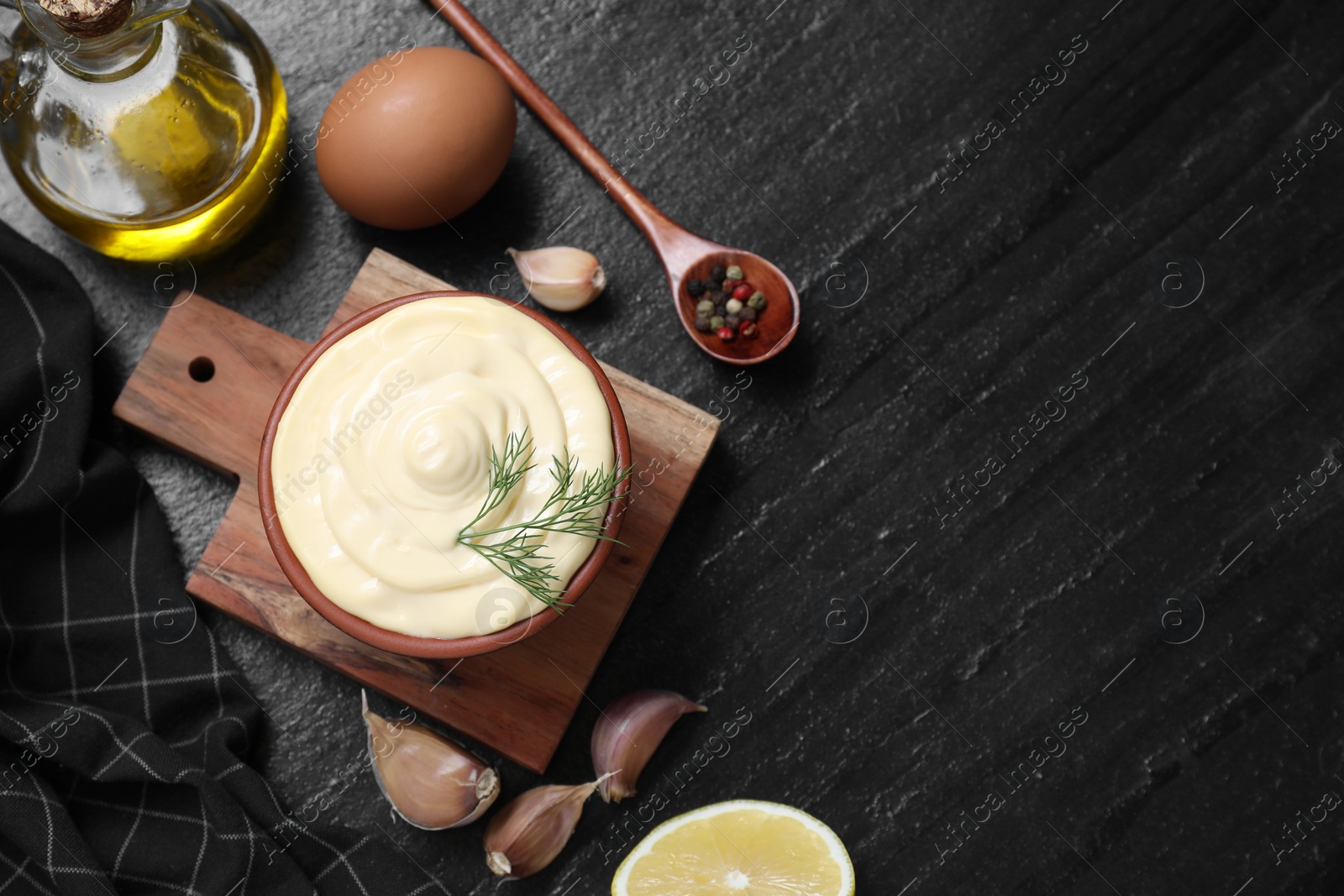 Photo of Fresh mayonnaise sauce in bowl and ingredients on black table, flat lay. Space for text