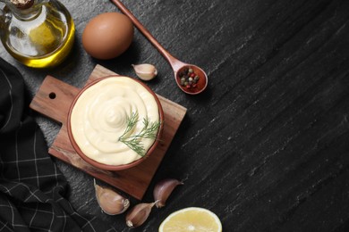 Photo of Fresh mayonnaise sauce in bowl and ingredients on black table, flat lay. Space for text