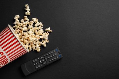 Photo of Modern tv remote control and popcorn on black background, flat lay. Space for text