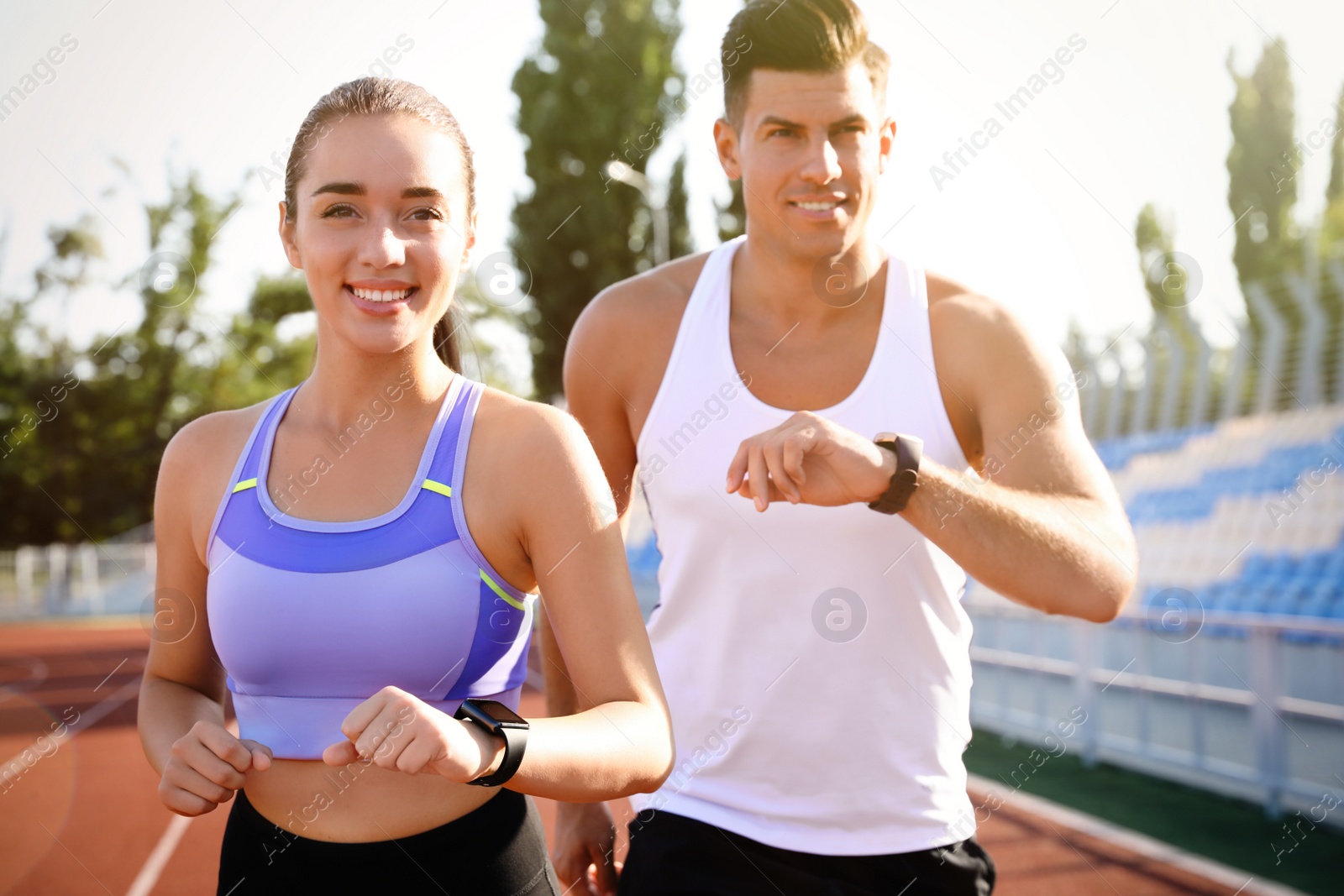 Photo of Couple with fitness trackers running at stadium