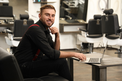 Photo of Young business owner with laptop in barber shop