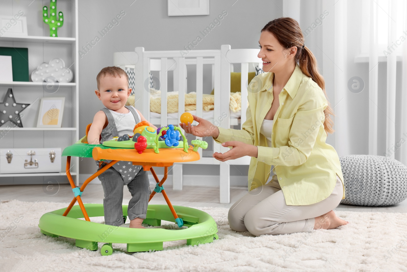 Photo of Mother and her little son spending time together at home. Cute baby making first steps with toy walker