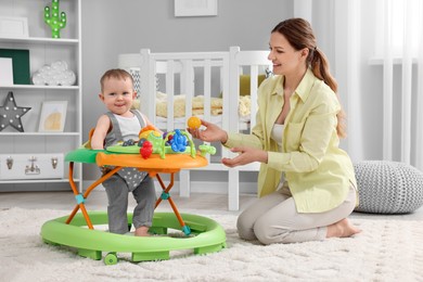 Photo of Mother and her little son spending time together at home. Cute baby making first steps with toy walker