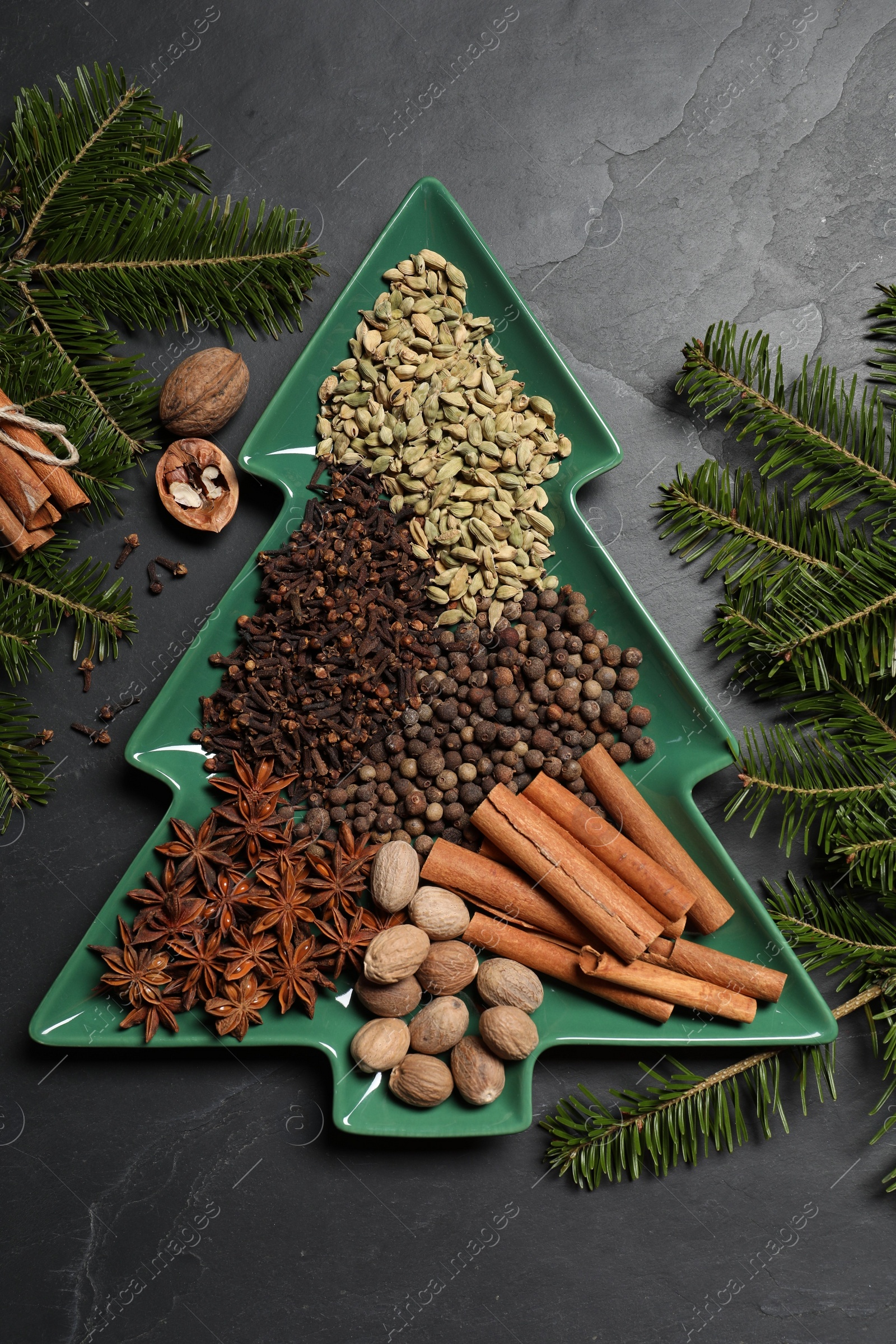 Photo of Different spices, nuts and fir branches on dark gray textured table, flat lay