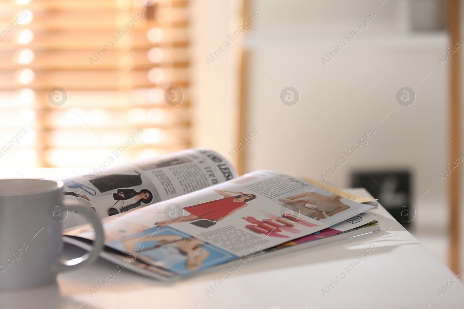 Photo of Fashion magazines and cup of hot drink on white table indoors