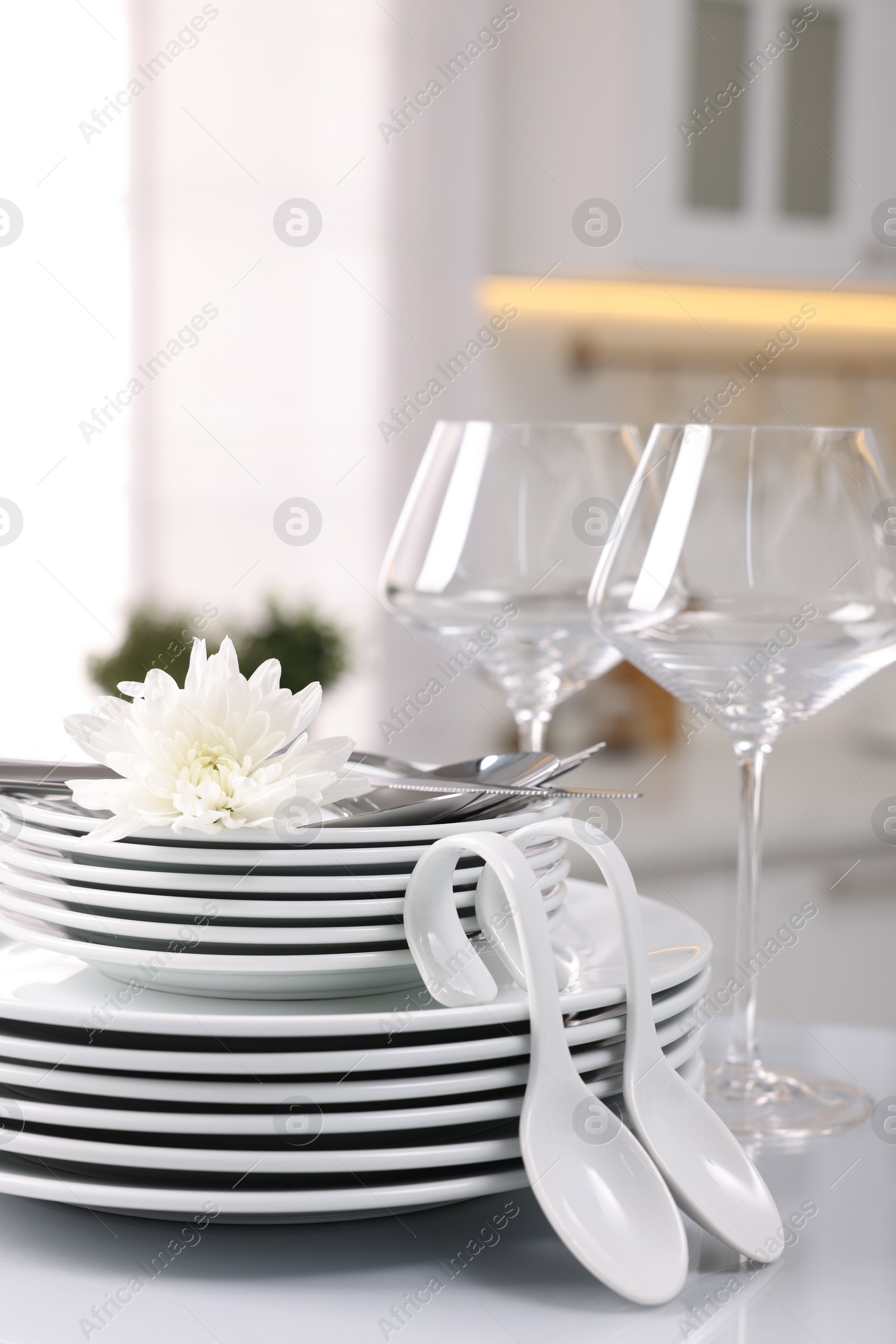 Photo of Set of clean dishware, glasses, cutlery and flower on table in kitchen