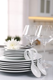 Set of clean dishware, glasses, cutlery and flower on table in kitchen