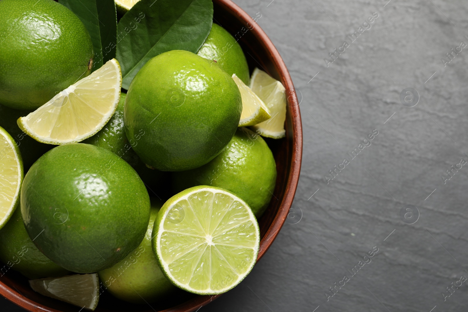 Photo of Fresh ripe limes in bowl on black table, top view. Space for text