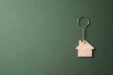 Wooden keychain in shape of house on dark green background, top view. Space for text