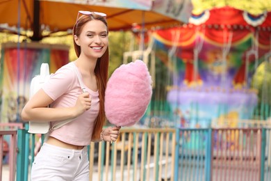 Smiling woman with cotton candy at funfair. Space for text