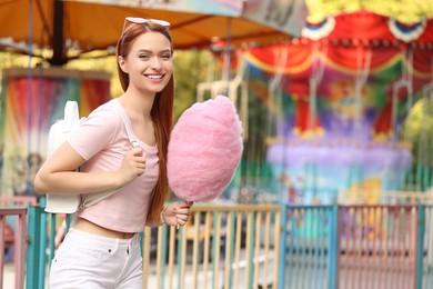 Photo of Smiling woman with cotton candy at funfair. Space for text