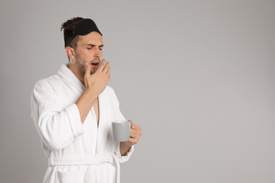 Sleepy young man in bathrobe on light grey background. Space for text