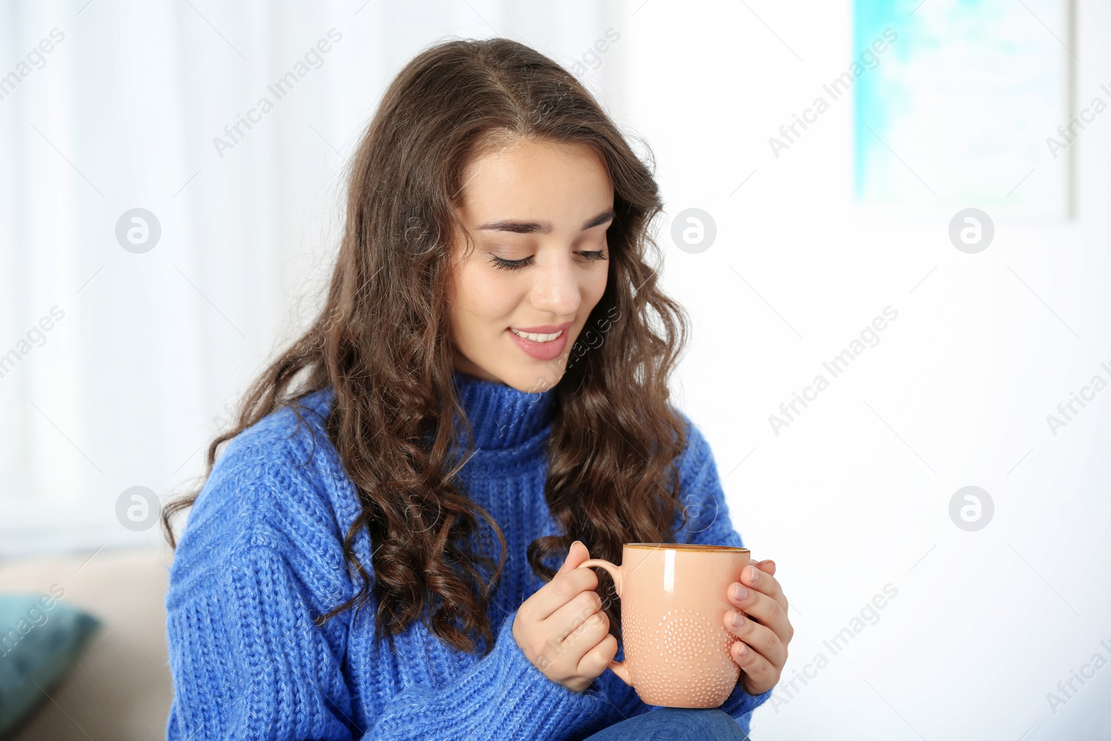 Photo of Young beautiful woman in warm sweater with cup of hot drink at home