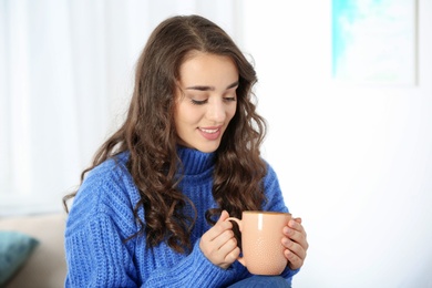 Photo of Young beautiful woman in warm sweater with cup of hot drink at home