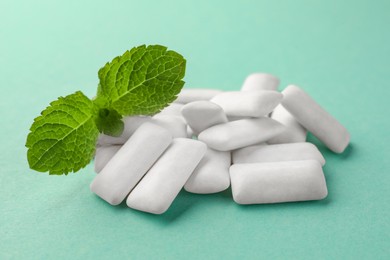 Photo of Tasty white chewing gums and mint leaves on turquoise background, closeup