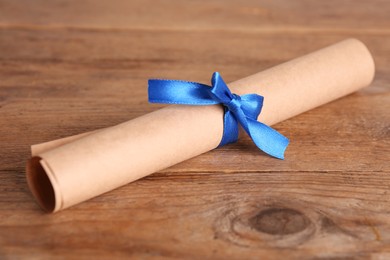 Photo of Rolled student's diploma with blue ribbon on wooden table