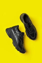 Photo of Stylish black sneakers on yellow background, flat lay