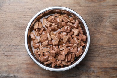 Photo of Wet pet food in feeding bowl on wooden table, top view