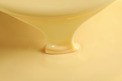 Photo of Tasty pouring condensed milk as background, closeup. Dairy product