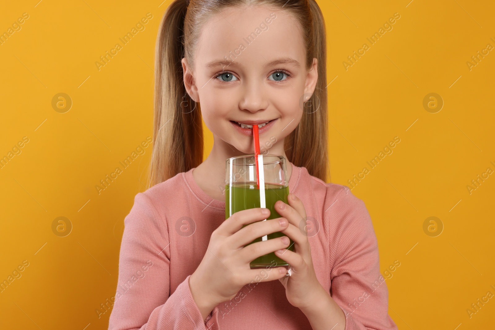 Photo of Cute little girl drinking fresh juice on orange background