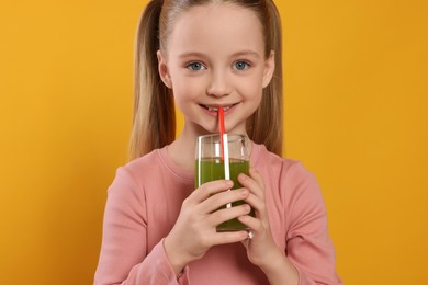 Photo of Cute little girl drinking fresh juice on orange background