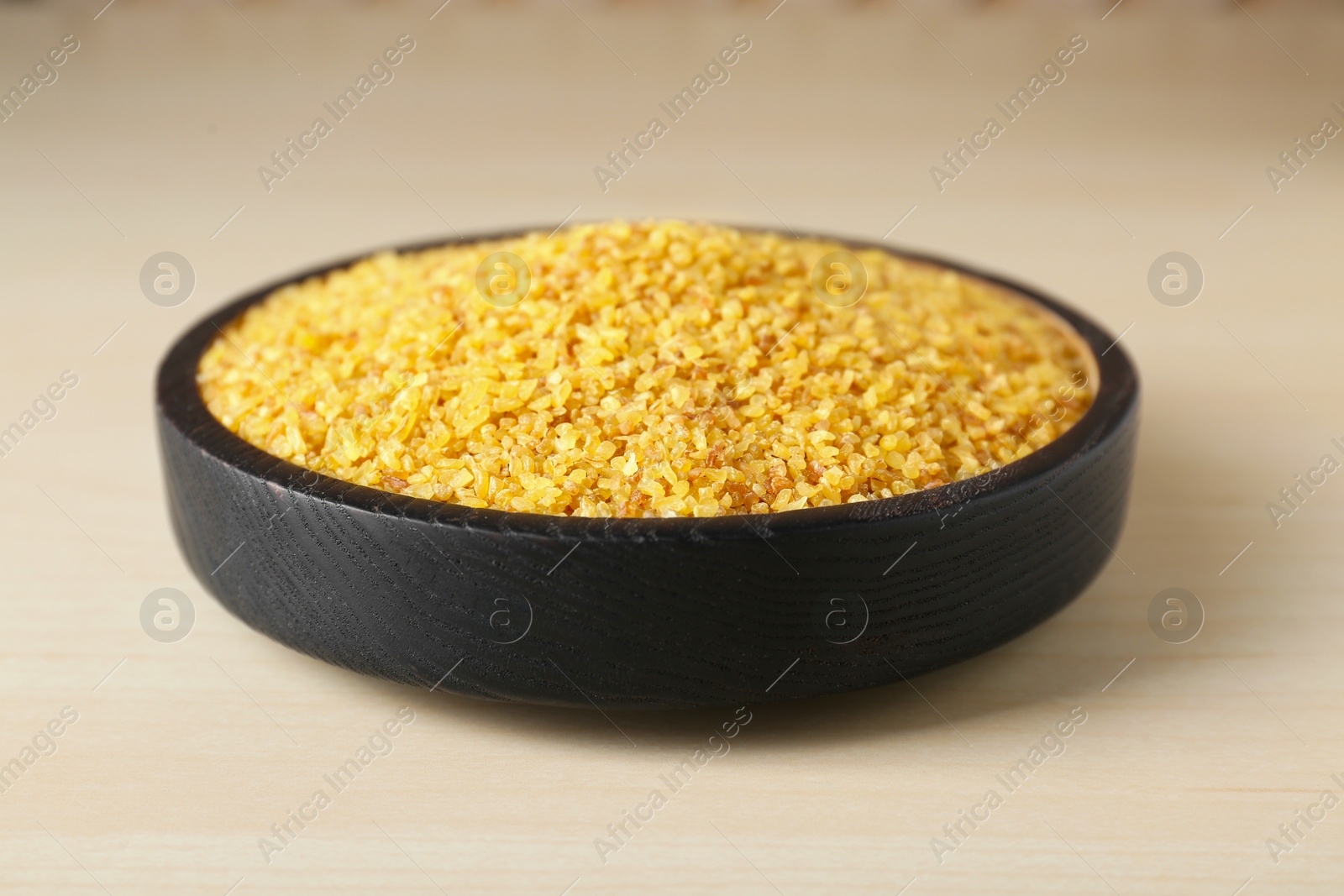 Photo of Bowl of uncooked bulgur on wooden table, closeup view