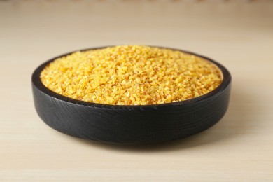 Bowl of uncooked bulgur on wooden table, closeup view