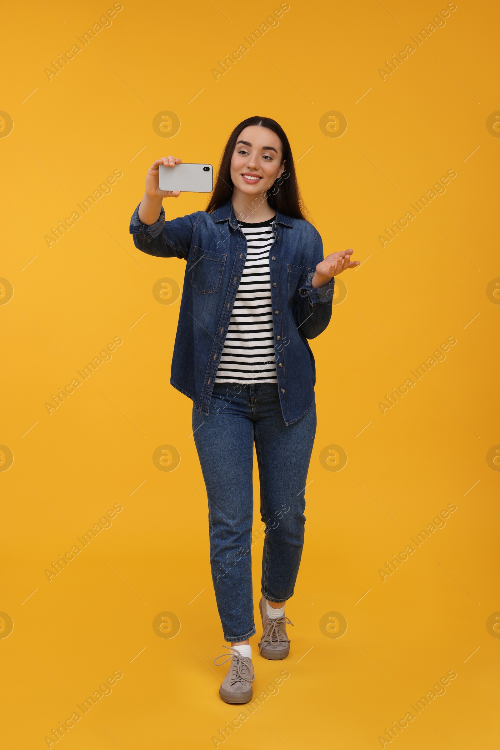 Photo of Smiling young woman taking selfie with smartphone on yellow background