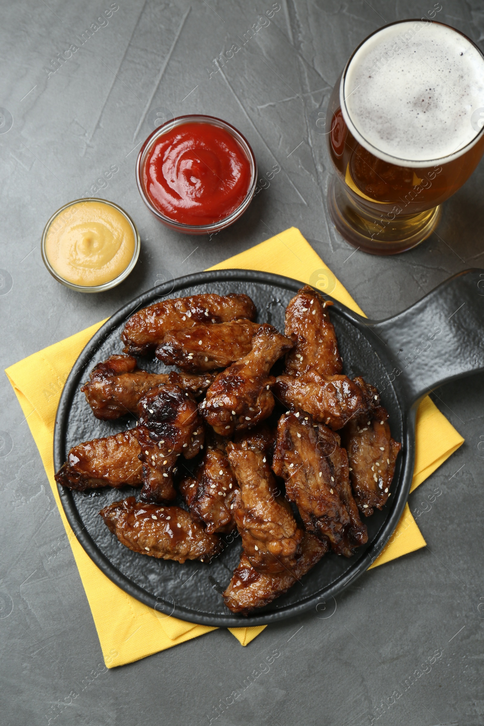Photo of Tasty roasted chicken wings, sauces and glass of beer on black table, flat lay