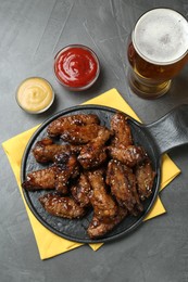 Tasty roasted chicken wings, sauces and glass of beer on black table, flat lay