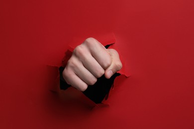 Photo of Man breaking through red paper with fist, closeup