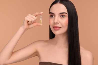 Photo of Beautiful young woman holding skincare ampoule on beige background