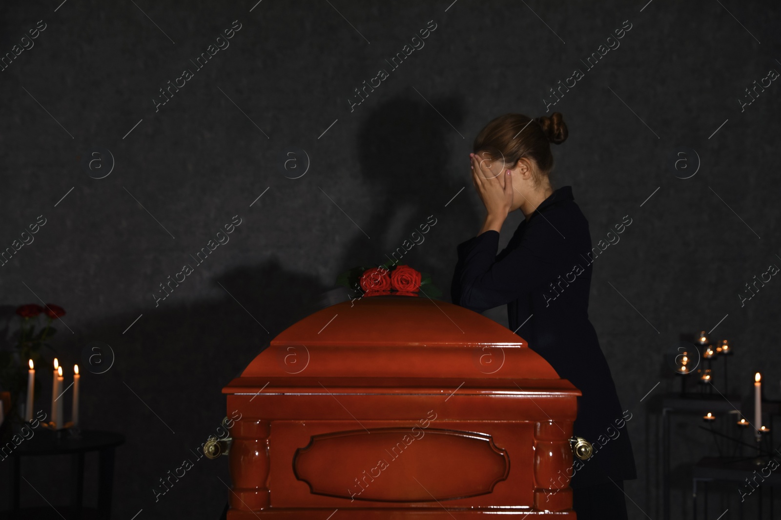 Photo of Sad young woman mourning near funeral casket with red roses in chapel