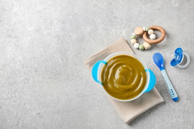 Photo of Flat lay composition with bowl of healthy baby food on grey table. Space for text