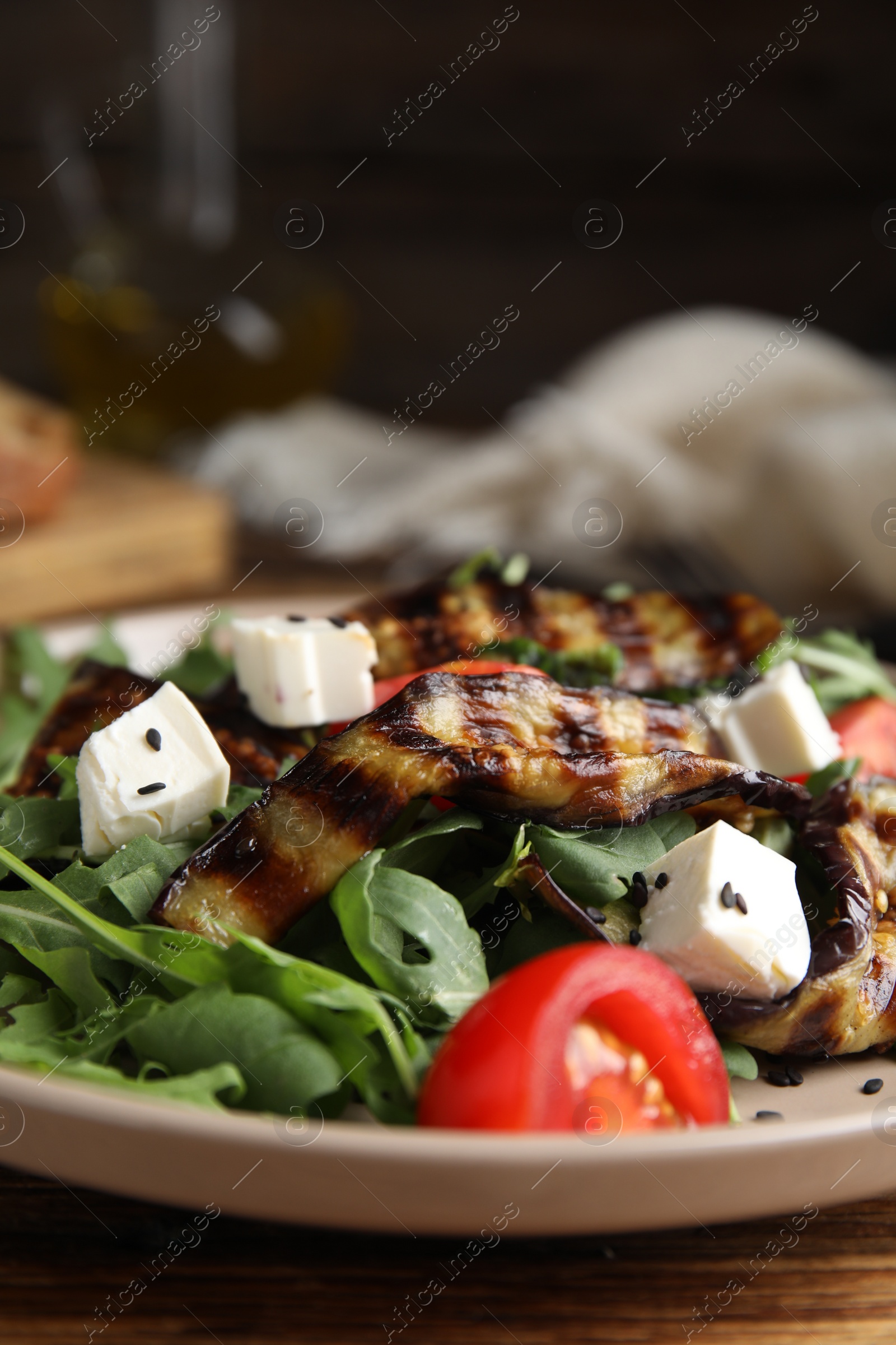 Photo of Delicious salad with roasted eggplant, feta cheese and arugula served on wooden table, closeup