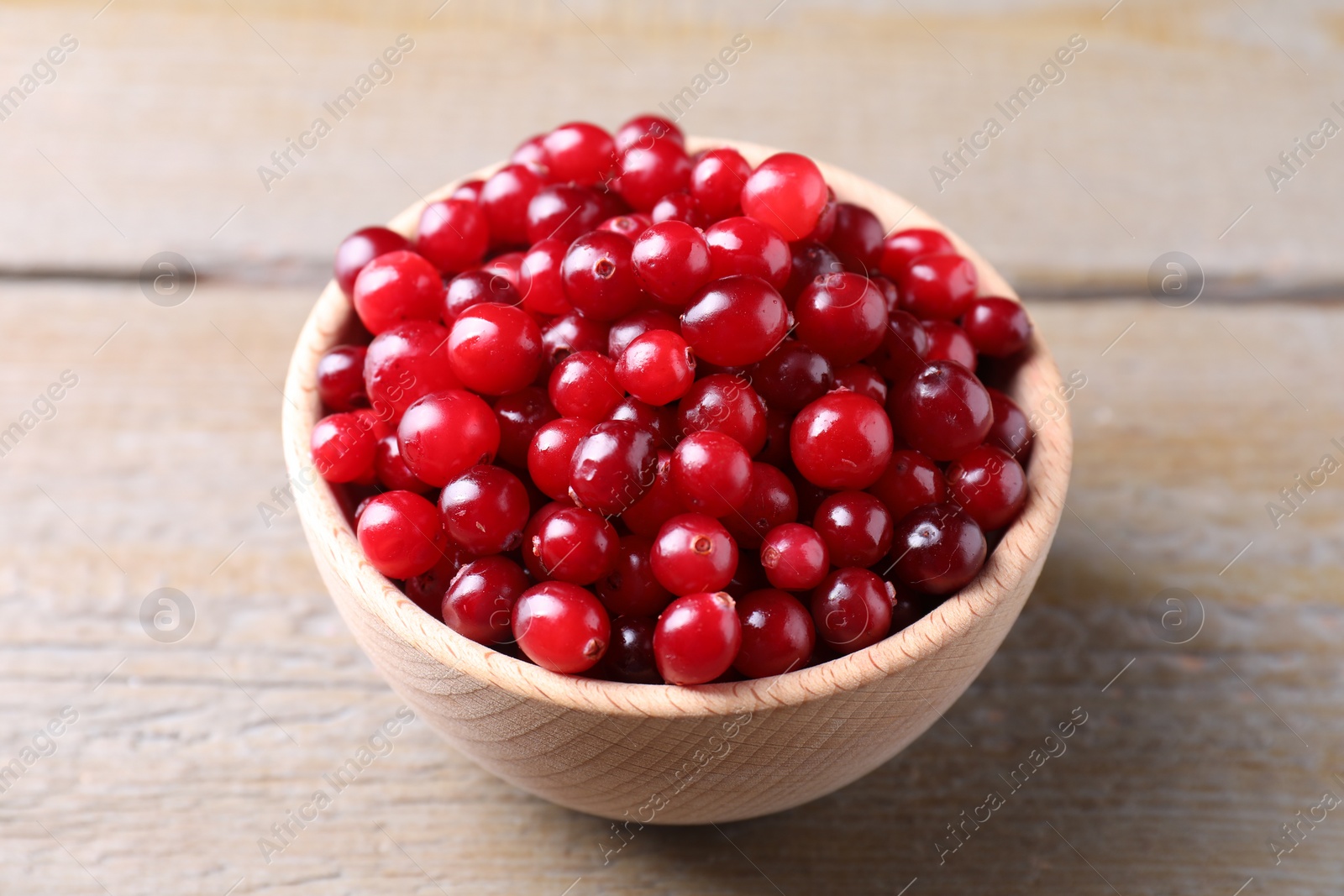 Photo of Fresh ripe cranberries in bowl on wooden table, closeup