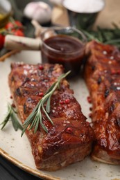 Photo of Tasty roasted pork ribs served with sauce and rosemary on table, closeup