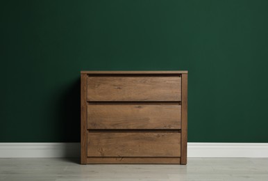 Photo of Modern wooden chest of drawers near green wall indoors