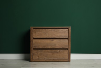 Modern wooden chest of drawers near green wall indoors