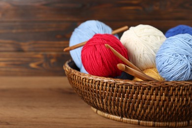 Photo of Wicker basket with clews of colorful knitting threads and crochet hooks on wooden table, closeup. Space for text