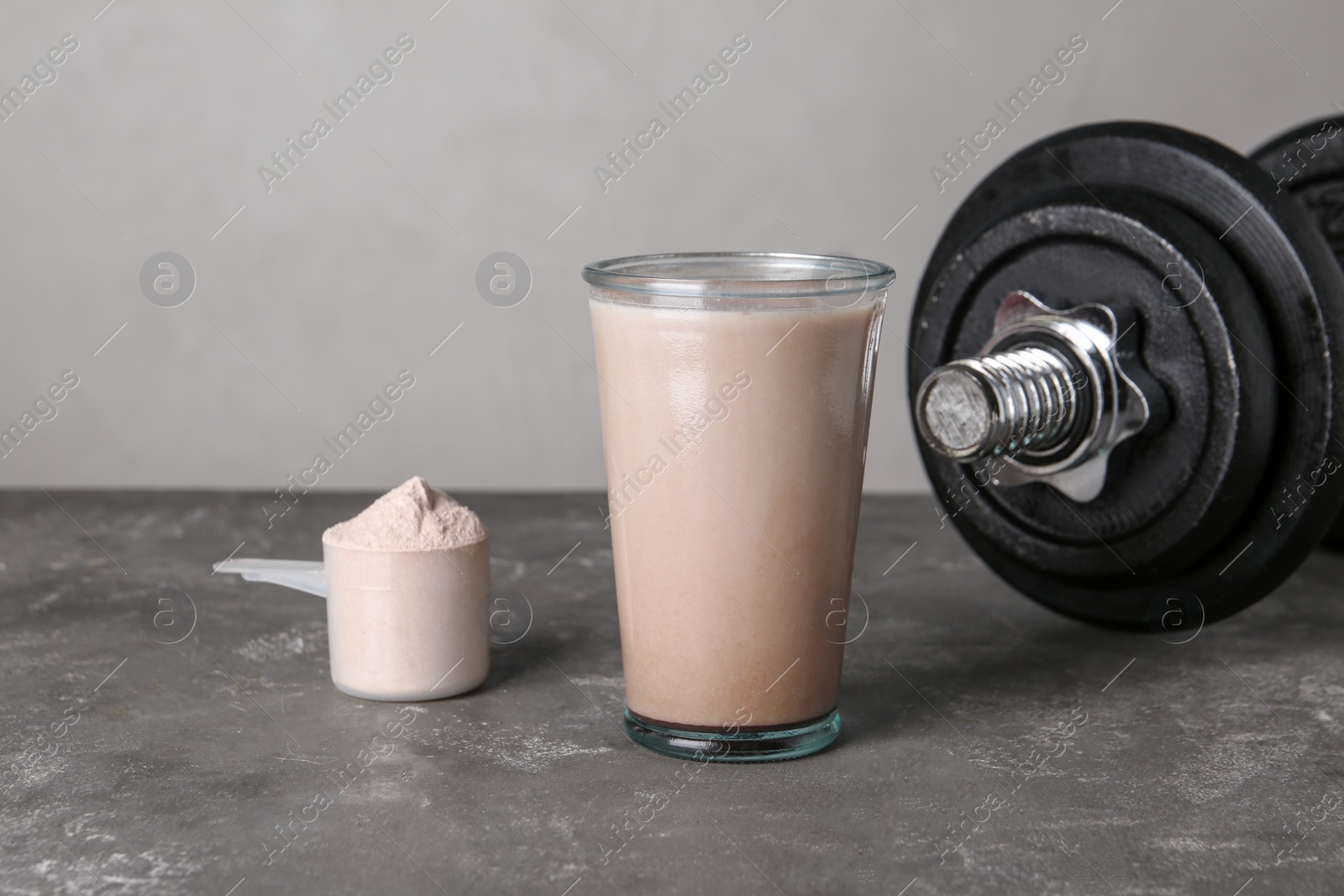 Photo of Glass with protein shake, scoop of powder and dumbbell on grey table