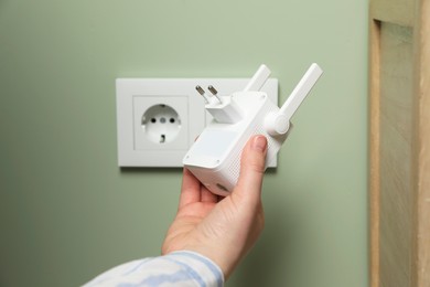 Woman holding wireless Wi-Fi repeater indoors, closeup