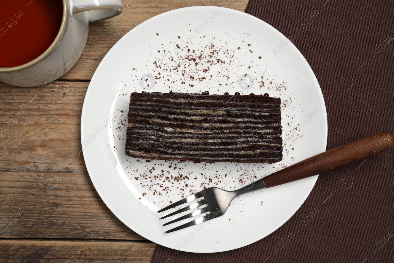 Photo of Plate with piece of tasty chocolate cake and fork on wooden table, top view