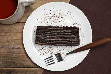 Plate with piece of tasty chocolate cake and fork on wooden table, top view