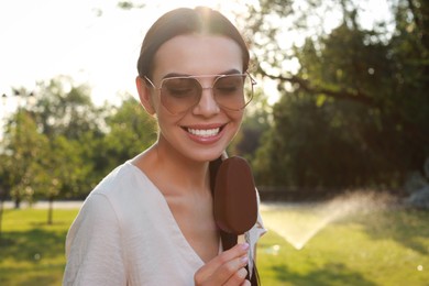 Photo of Beautiful young woman holding ice cream glazed in chocolate outdoors